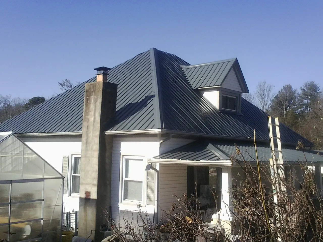 Dark blue standing seam metal roof on a white farmhouse with dormer — Slate & Tile Roof Repair by Roofing Brothers in Kelley