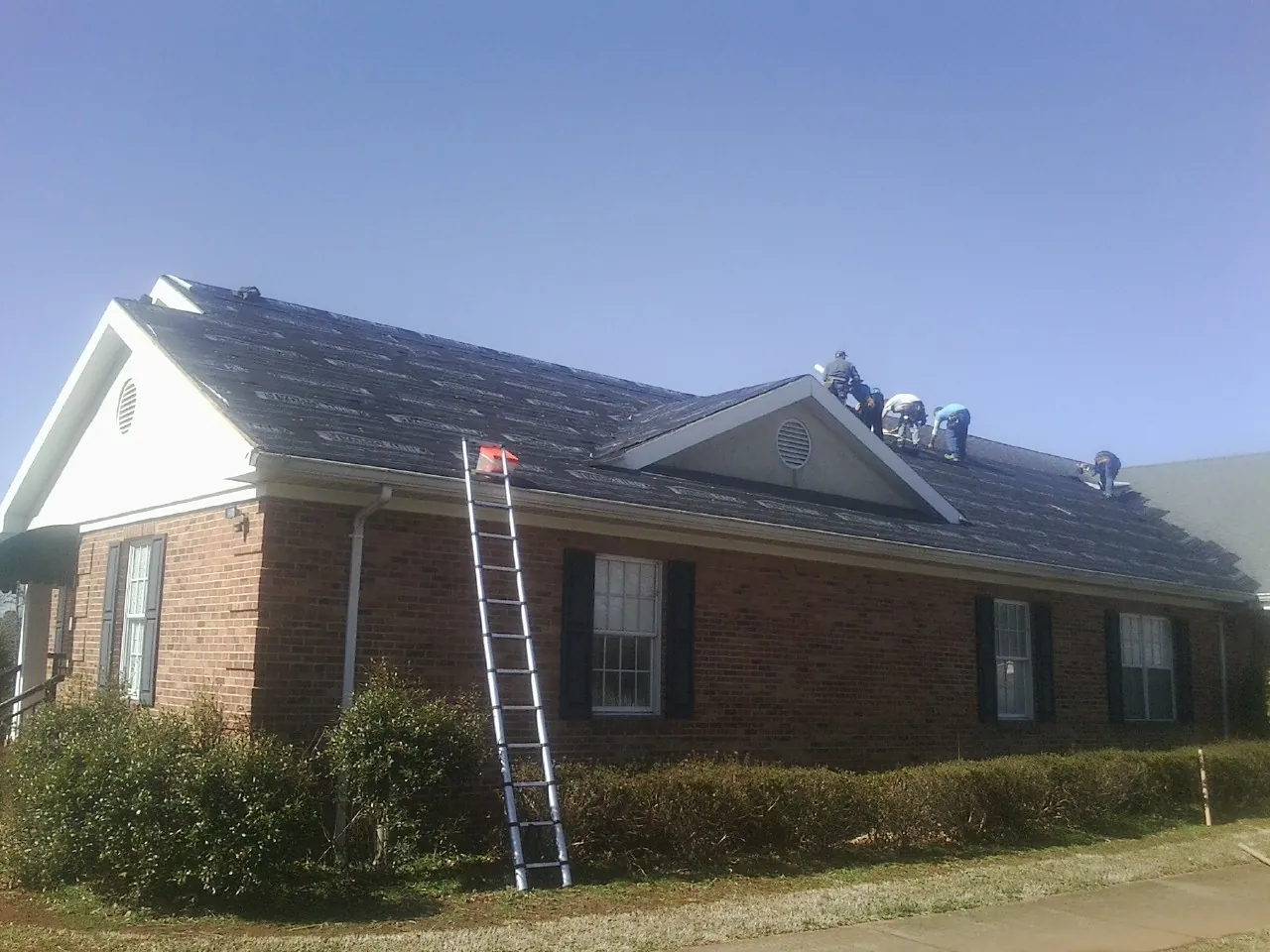 Crew tearing shingles off a brick ranch roof with a ladder set — Emergency Roof Repair work by our crew in Kelley