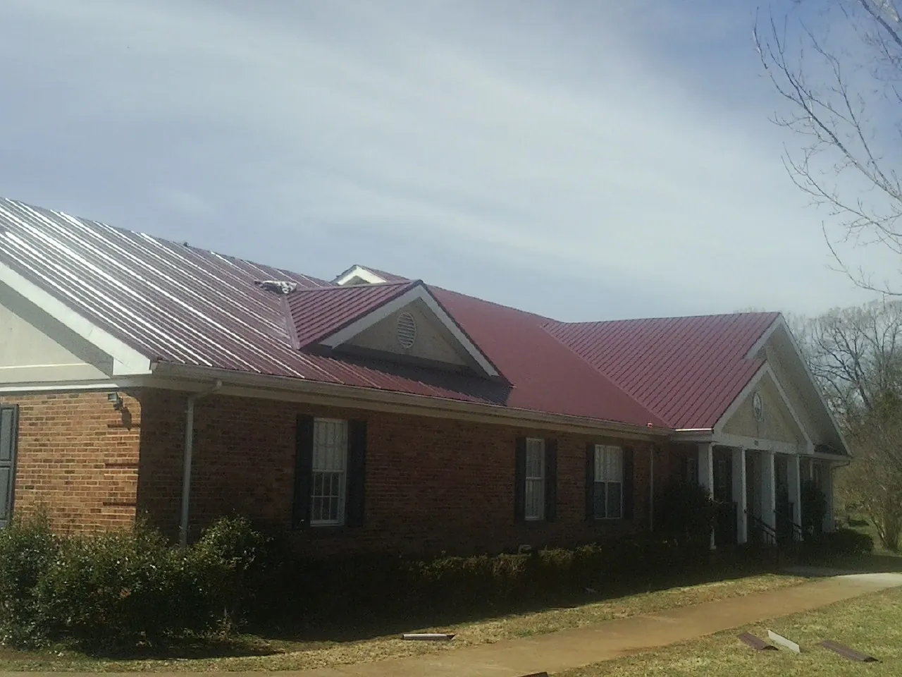 Red metal roof with gabled entries on a long brick building, from a Hail Damage Roof Repair job in Kelley