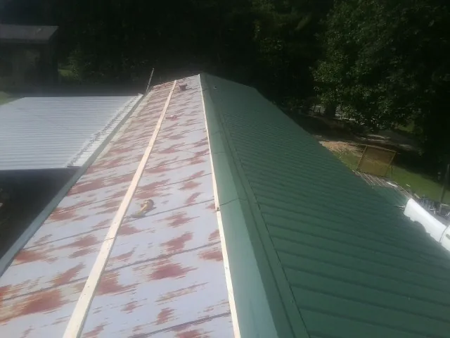 Old rusted panels beside newly installed green metal roofing — Wind Damage Roof Repair by Roofing Brothers in Kelley