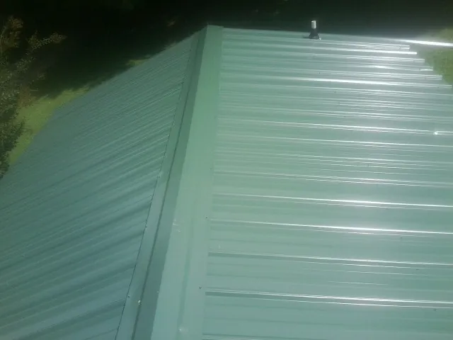 New green metal panels meeting at the ridge of a roof — Flat Roof Repair work by our crew in Kelley