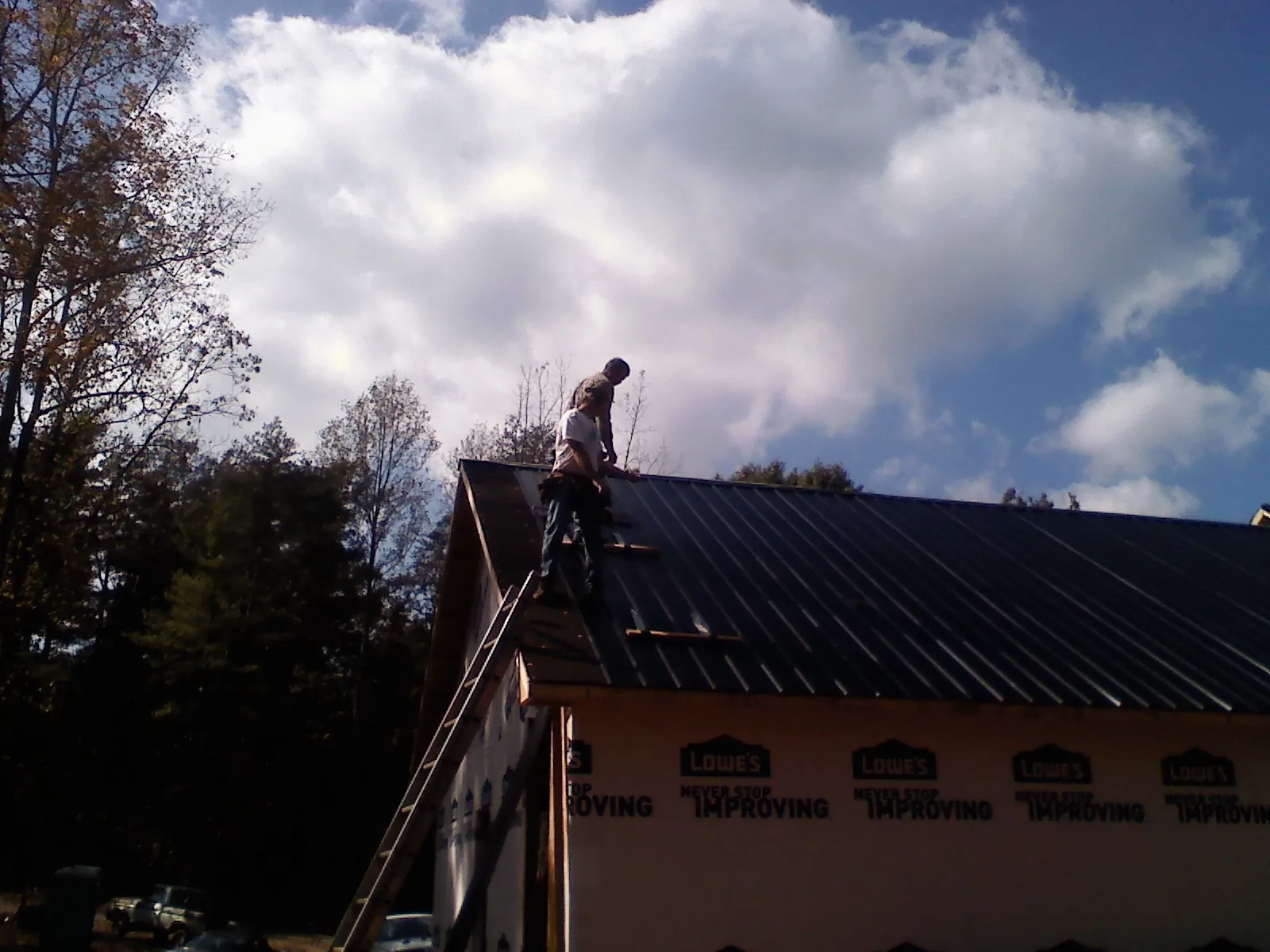 Roofer fastening dark metal panels high against a cloudy sky, from a Roof Inspection job in Kelley