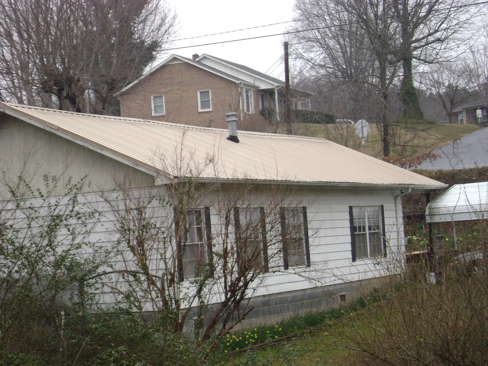 Tan metal roof on a white sided house set into a hillside — Commercial Roofing by Roofing Brothers in Kelley