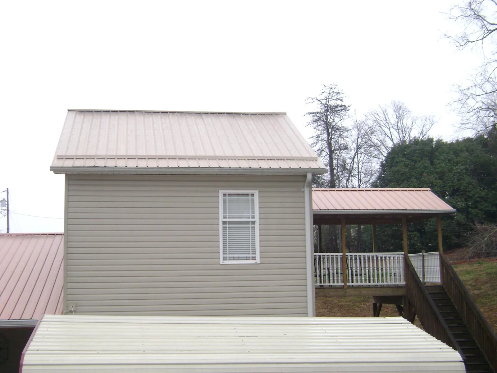 Tan metal roofs on a two story addition and attached porch, from a Roof Replacement job in Kelley